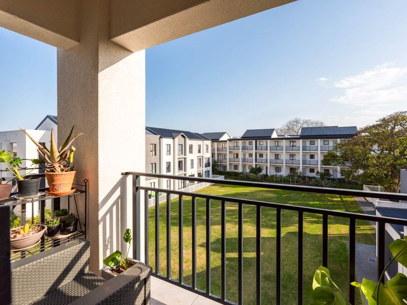 A covered balcony featuring a metal balustrade, overlooking a communal garden area within the apartment complex.