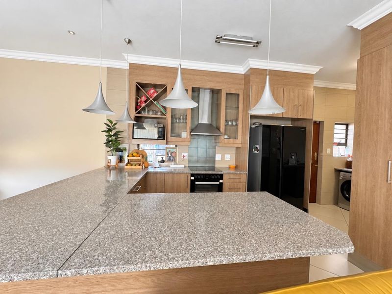 Modern kitchen featuring wood-finish cabinetry, granite countertops, a built-in oven with extractor fan, and a breakfast bar area.