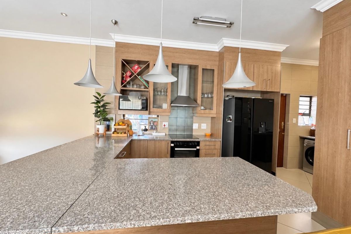 Modern kitchen featuring wood-finish cabinetry, granite countertops, a built-in oven with extractor fan, and a breakfast bar area.