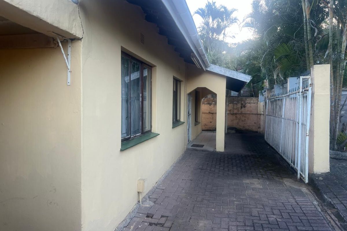 Side exterior view of the townhouse featuring a paved walkway, metal security gate, and perimeter retaining wall with visible signs of wear.