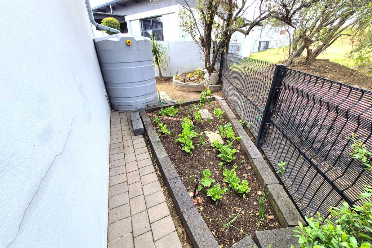 A side garden area featuring a raised planter bed, paved walkway, and a rainwater collection tank against the exterior wall of the townhouse.