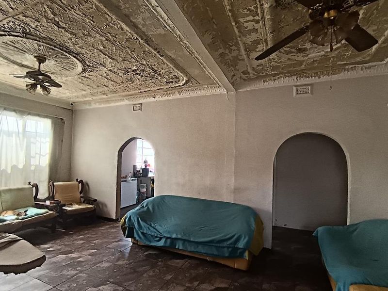 Spacious living room featuring original ornate plaster ceilings, arched doorways, and tiled flooring, currently requiring significant restoration and cosmetic updates.
