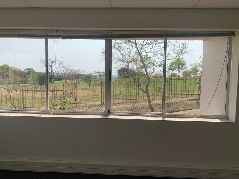An office space featuring a large window with views of the surrounding landscape and perimeter fencing.