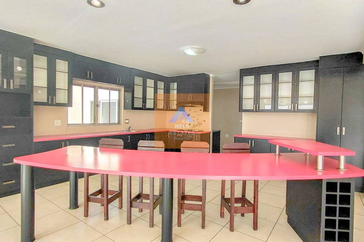 Spacious kitchen featuring dark cabinetry, contrasting pink countertops, a built-in breakfast bar, and tiled flooring.