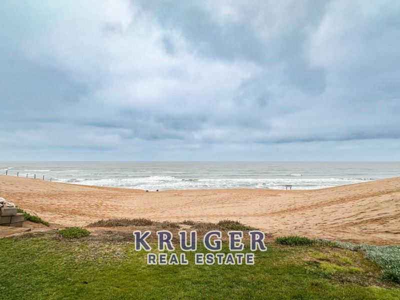 A scenic view of the beach and ocean from the property, featuring a natural dune landscape and a stone retaining wall.