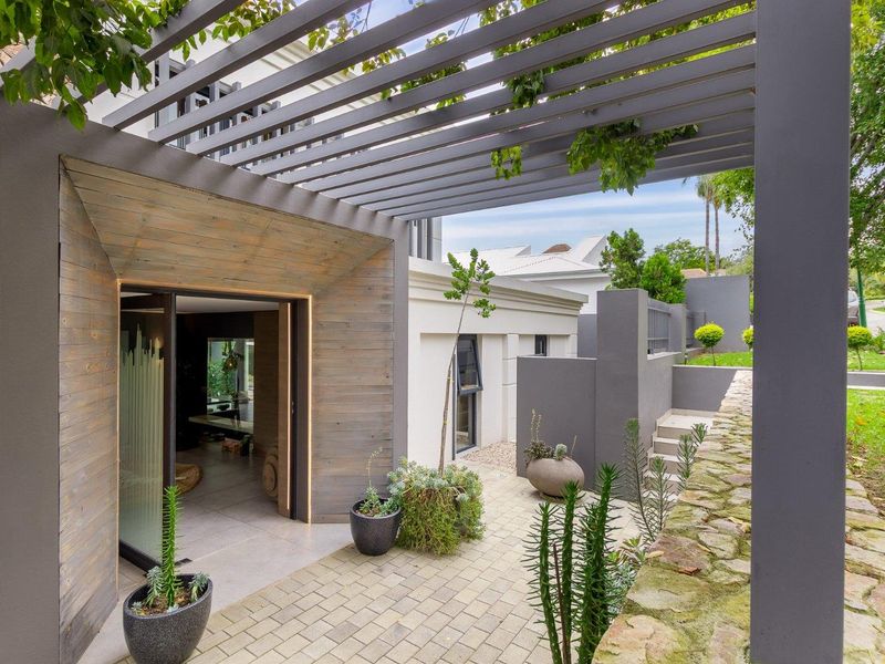 A modern outdoor patio area featuring a timber pergola, stone retaining wall, and stylish timber-clad entrance leading into the home.
