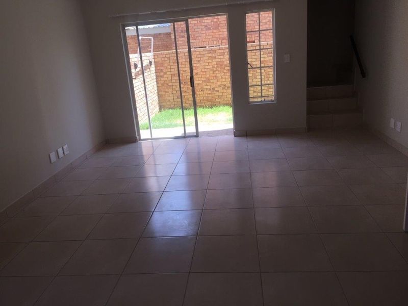 An empty, open-plan living area featuring neutral tiled flooring, a staircase, and sliding glass doors providing access to the rear garden.