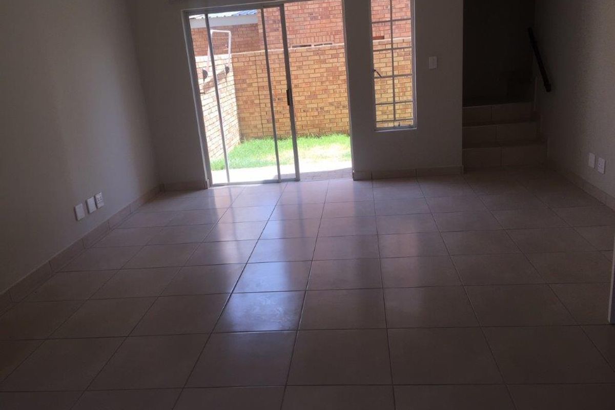 An empty, open-plan living area featuring neutral tiled flooring, a staircase, and sliding glass doors providing access to the rear garden.