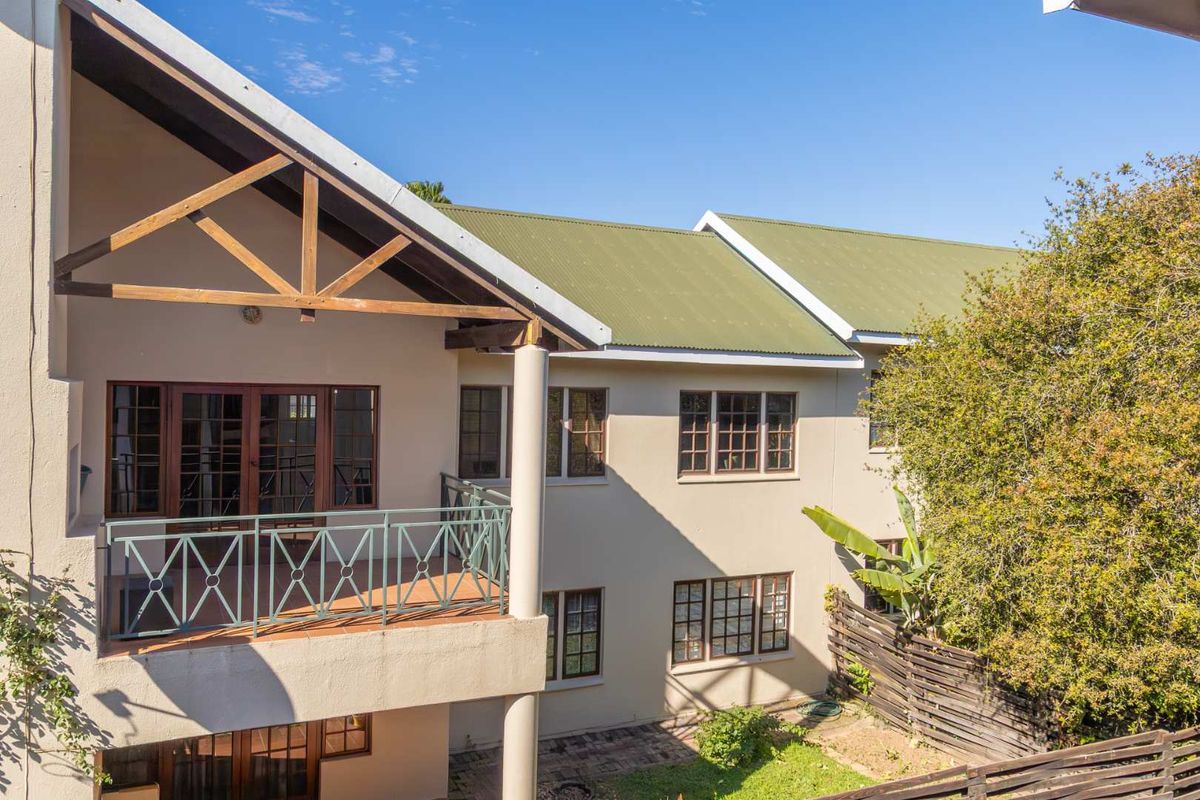 Exterior view of the apartment building featuring a covered balcony with timber truss detailing, green metal roofing, and multi-pane windows.