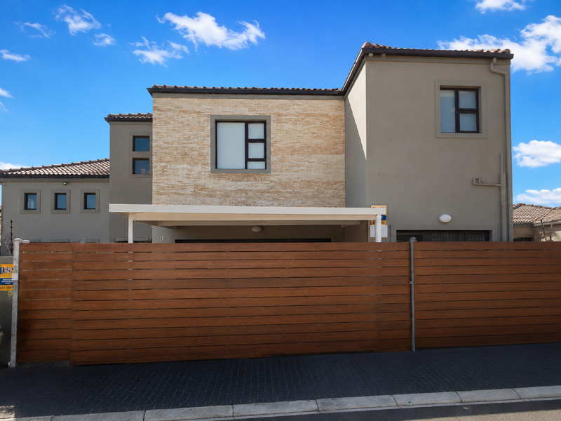 Modern double-storey residential home featuring a timber slat gate, stone cladding accents, and a paved driveway with a covered carport.