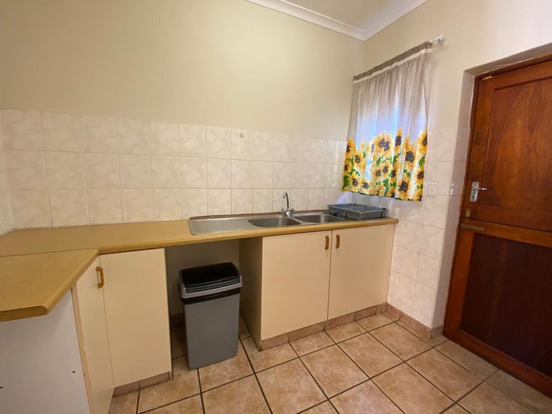 Functional scullery area featuring a stainless steel double sink, laminate countertops, built-in cabinetry, and ceramic tile finishes.