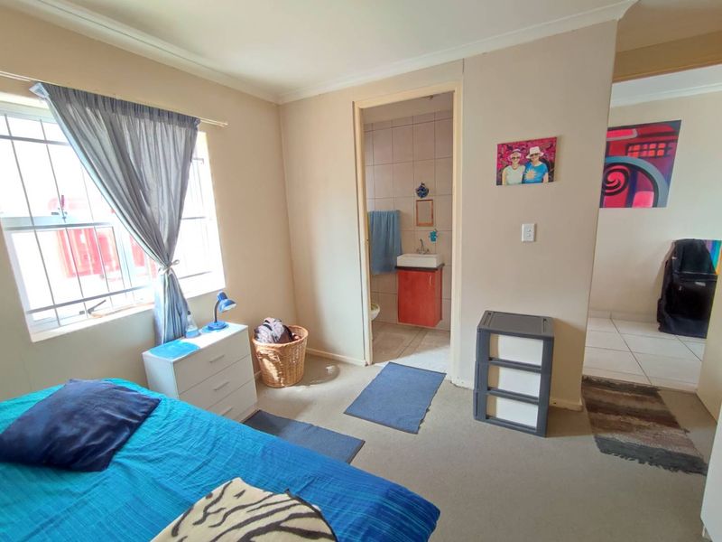 A bedroom featuring neutral walls, carpeted flooring, security bars on the window, and an adjoining en-suite bathroom with a vanity basin.