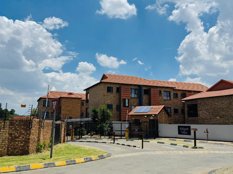 Front entrance view of Ashanti Villas complex featuring face brick architecture, tiled roofing, solar panels, and secure gated access.