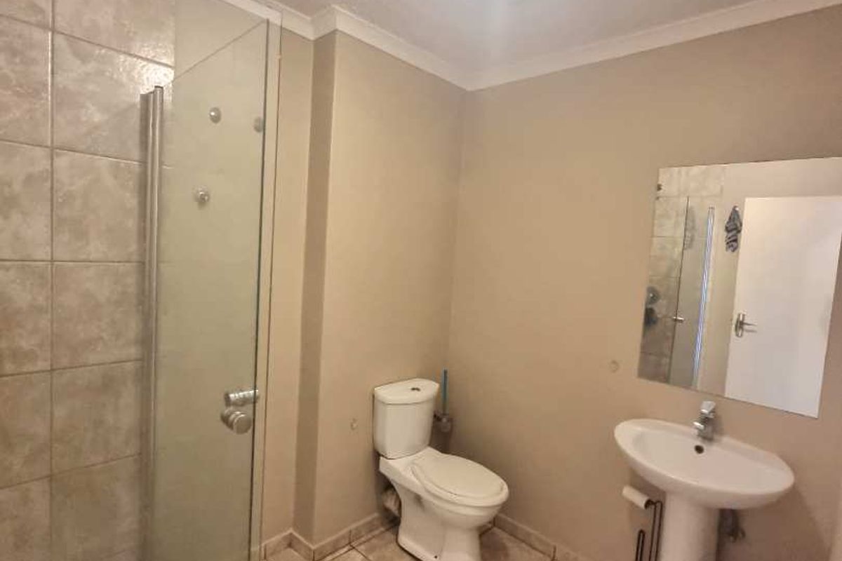 A functional bathroom featuring a glass-enclosed shower, pedestal basin, and toilet with neutral wall finishes and tiled flooring.
