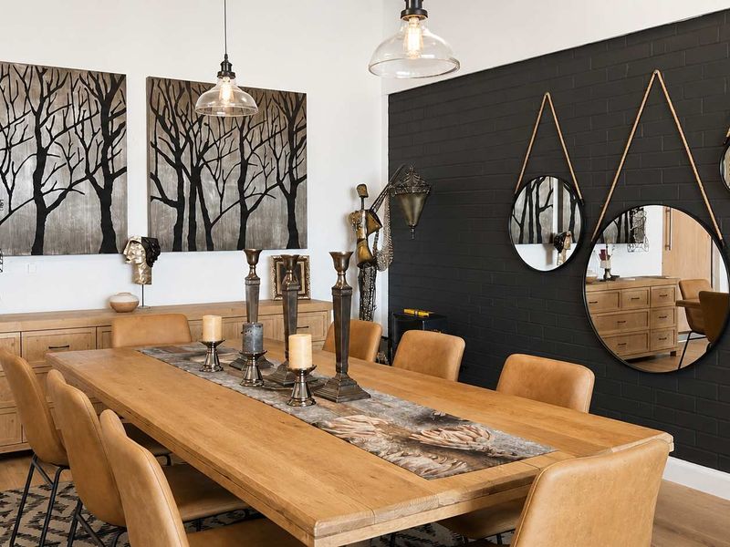 A well-appointed dining room featuring a striking black painted brick feature wall, modern pendant lighting, and high-quality laminate flooring.