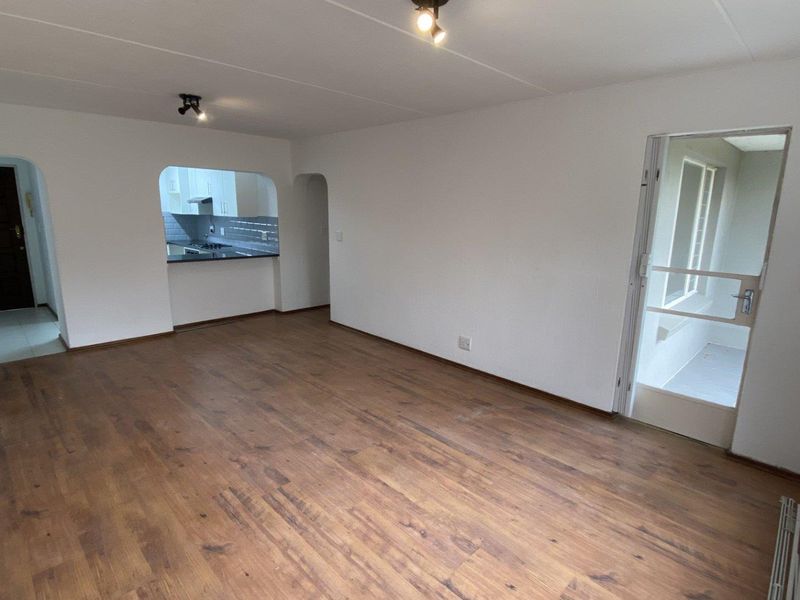 Spacious open-plan living area featuring laminate flooring, neutral walls, and a convenient pass-through window connecting to the kitchen.