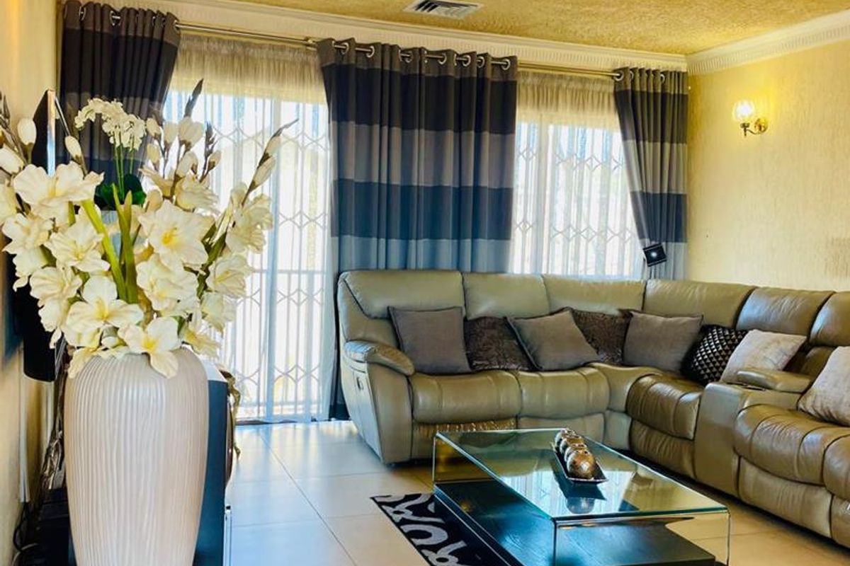 A comfortable living room featuring tiled flooring, air conditioning, and large sliding glass doors with security gates, providing access to the exterior.