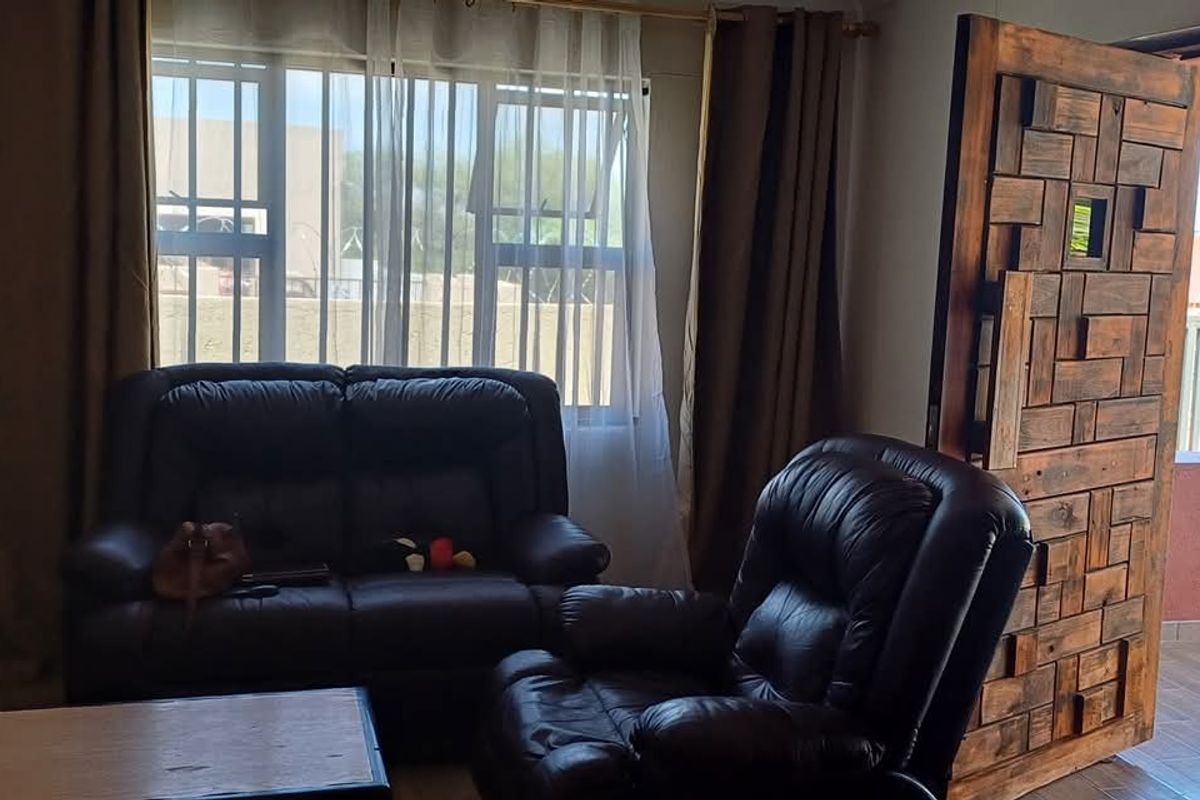 A living room featuring a large window with natural light and a distinctive textured wooden door leading to an outdoor patio area.