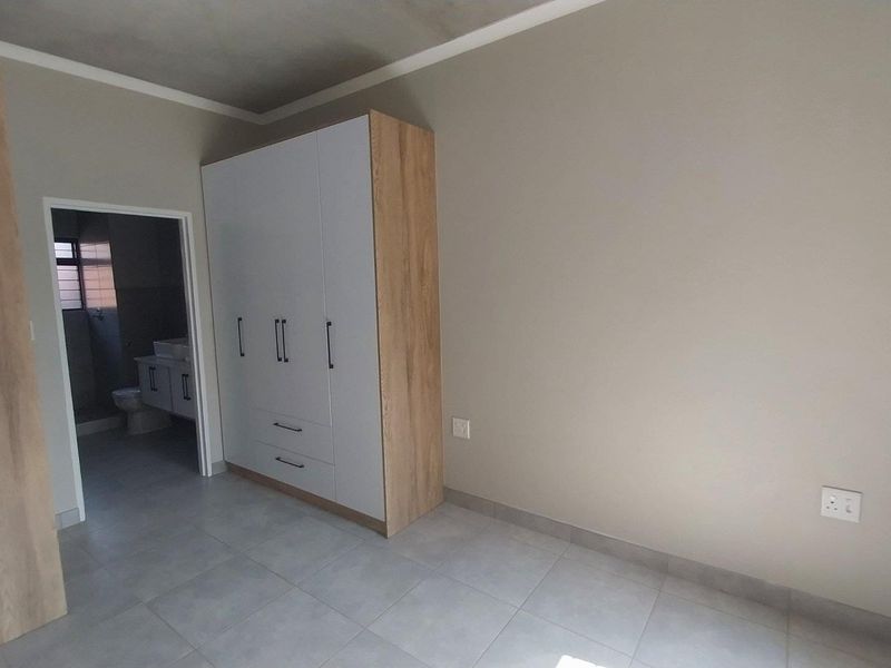 A clean, modern bedroom featuring neutral tiled floors, built-in cabinetry, and an en-suite bathroom entrance.