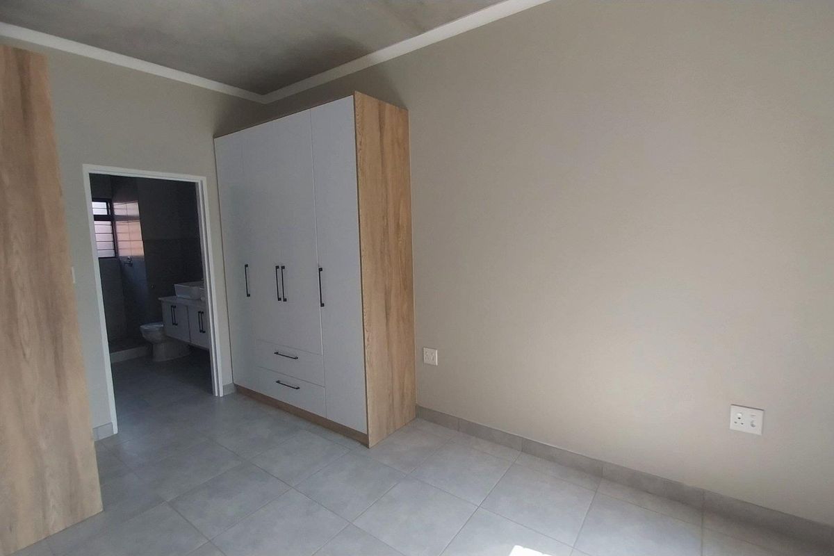 A clean, modern bedroom featuring neutral tiled floors, built-in cabinetry, and an en-suite bathroom entrance.
