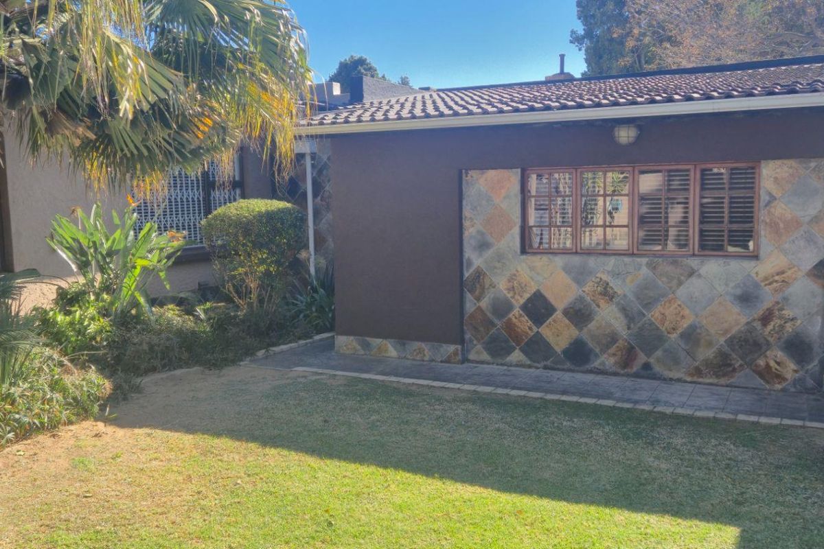 Rear exterior view of the property featuring a tiled roof, slate wall accents, and a landscaped garden area with a paved walkway.