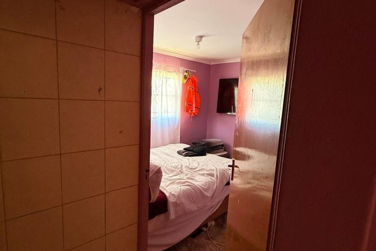A view through a doorway into a bedroom featuring purple walls and a window with security bars.