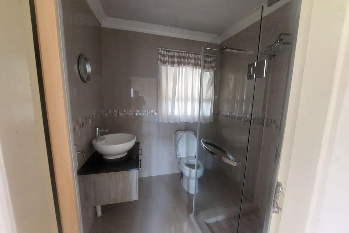 A modern bathroom featuring a vessel sink on a vanity cabinet, a glass-enclosed shower with a rain shower head, and neutral wall tiling.