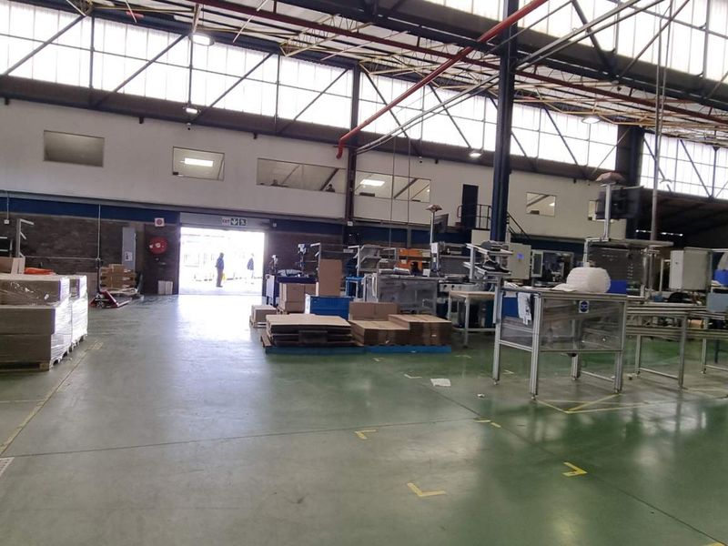 Spacious industrial warehouse facility featuring high ceilings, exposed steel trusses, large clerestory windows for natural light, and painted concrete flooring.