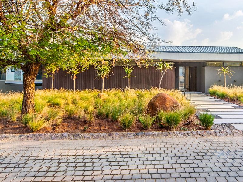 Modern front facade featuring timber cladding, a metal roof, and a well-maintained landscaped garden with a stone pathway leading to the entrance.