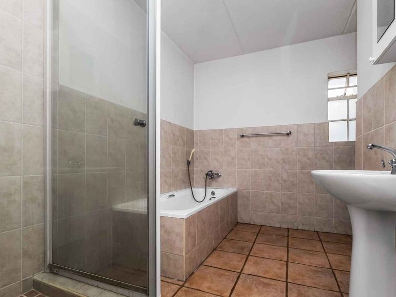 A functional bathroom featuring a pedestal basin, a built-in bathtub, and a separate shower enclosure with neutral wall and floor tiling.