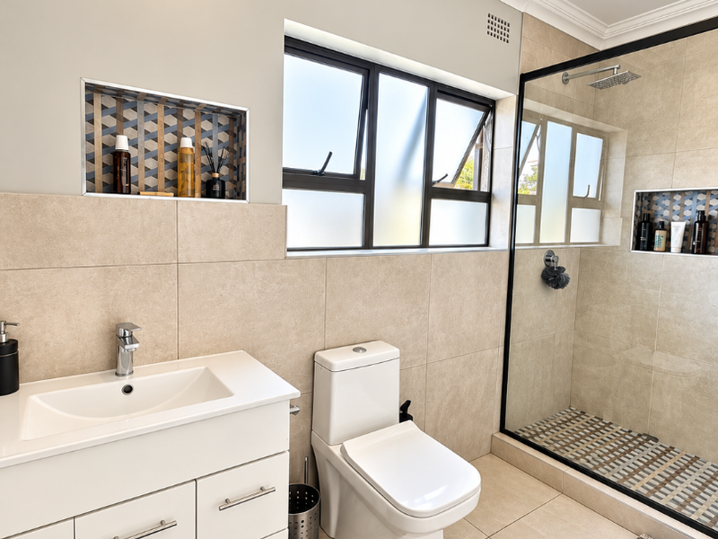 Modern bathroom featuring a vanity cabinet, walk-in shower with glass screen, recessed wall niches, and neutral floor-to-ceiling tiling.