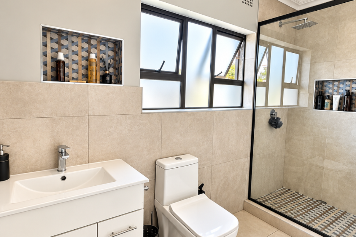 Modern bathroom featuring a vanity cabinet, walk-in shower with glass screen, recessed wall niches, and neutral floor-to-ceiling tiling.