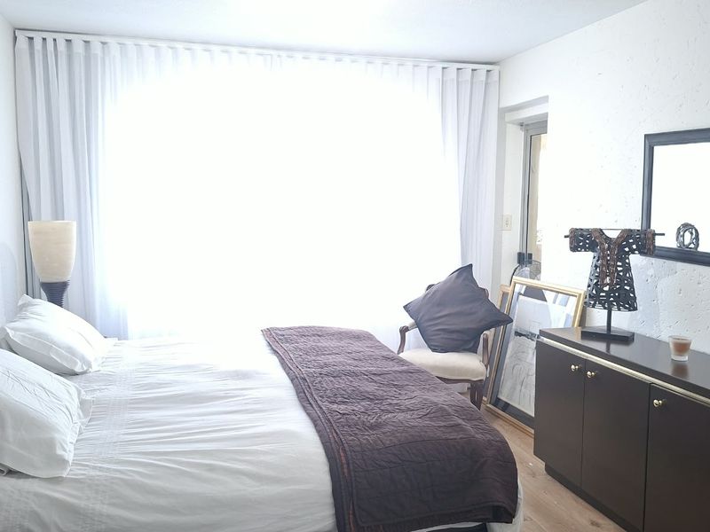 A well-lit bedroom featuring laminate flooring, textured walls, and floor-to-ceiling curtain tracks, creating a comfortable and bright living space.