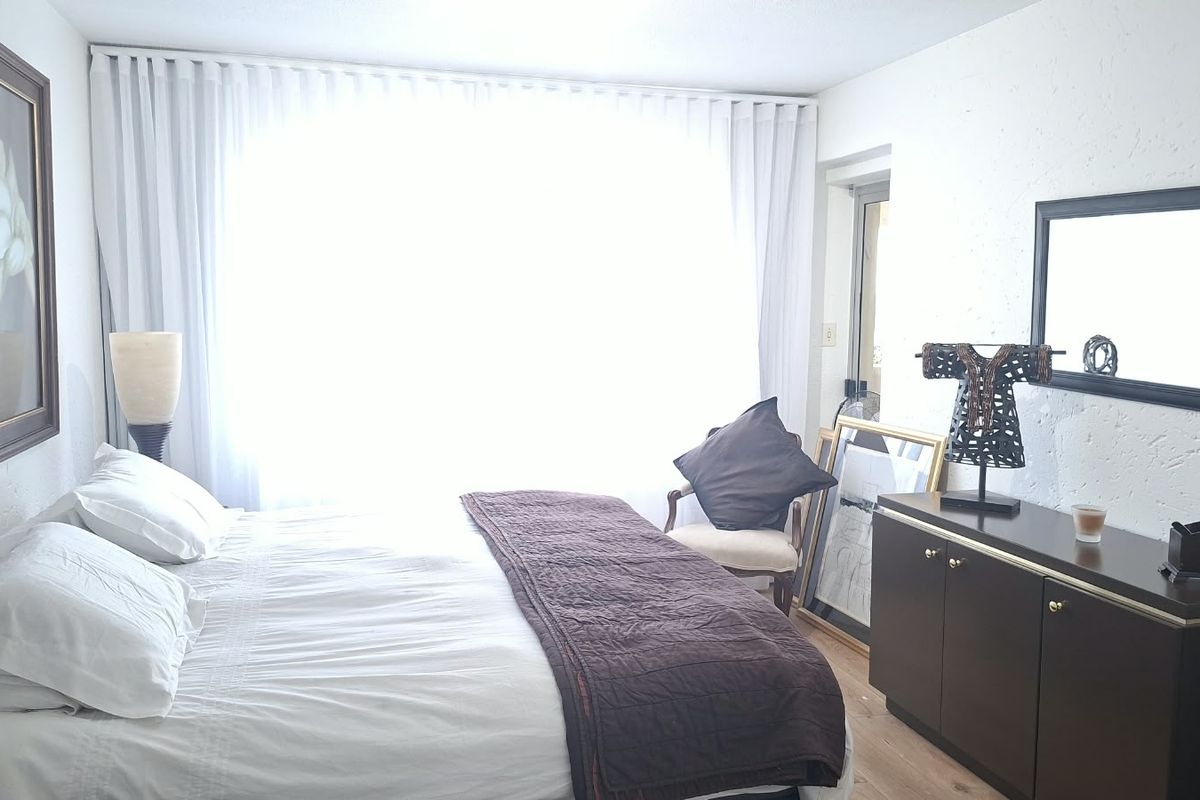 A well-lit bedroom featuring laminate flooring, textured walls, and floor-to-ceiling curtain tracks, creating a comfortable and bright living space.