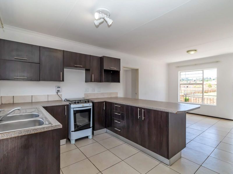 Open-plan kitchen and living area featuring dark wood cabinetry, laminate countertops, a double sink, and ceramic floor tiles throughout.