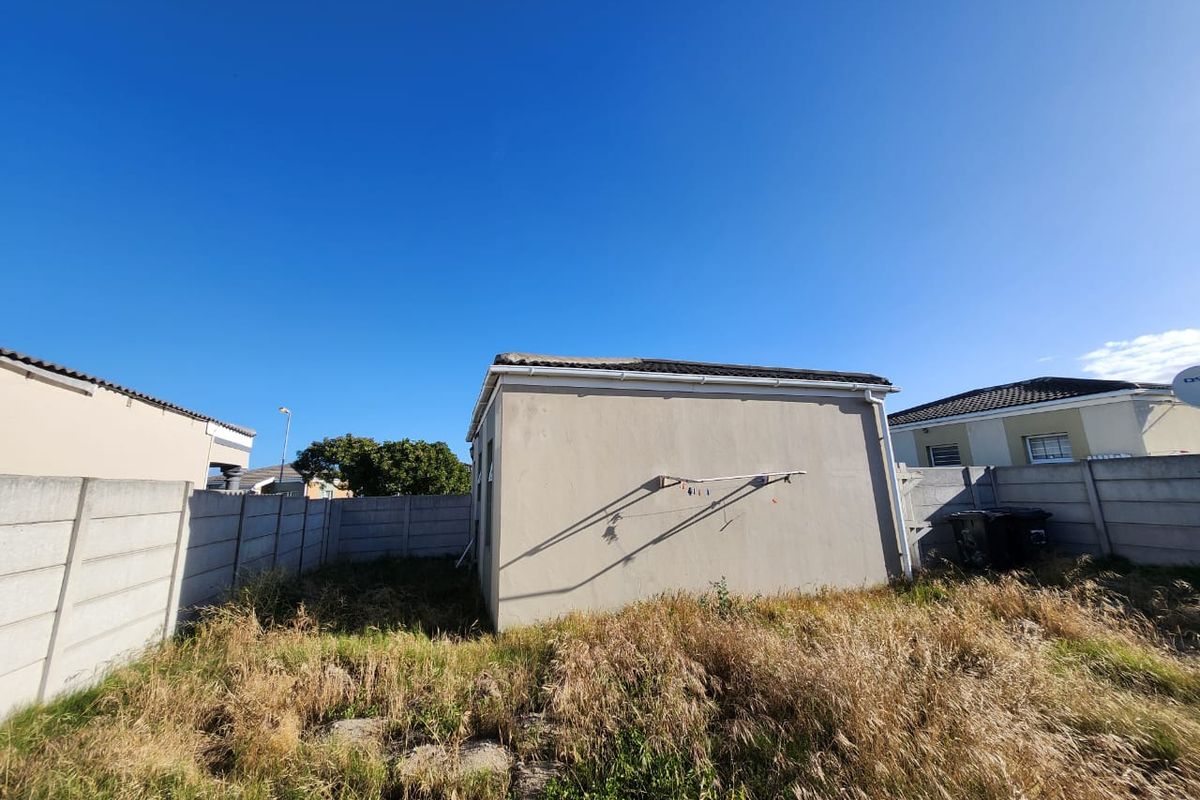 Rear view of the property showing a detached structure, precast concrete boundary walls, and an overgrown garden area.