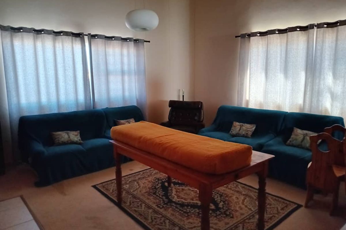 A spacious living room featuring neutral walls, carpeted flooring, and large windows with curtains, providing a comfortable and functional living space.
