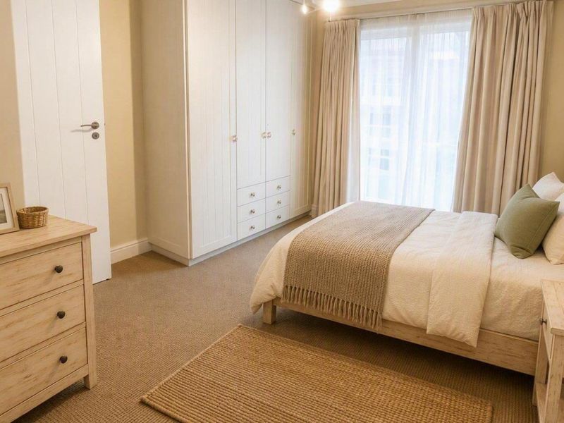 A well-maintained bedroom featuring neutral carpet flooring, ample built-in wardrobe storage, and a sliding glass door providing natural light.