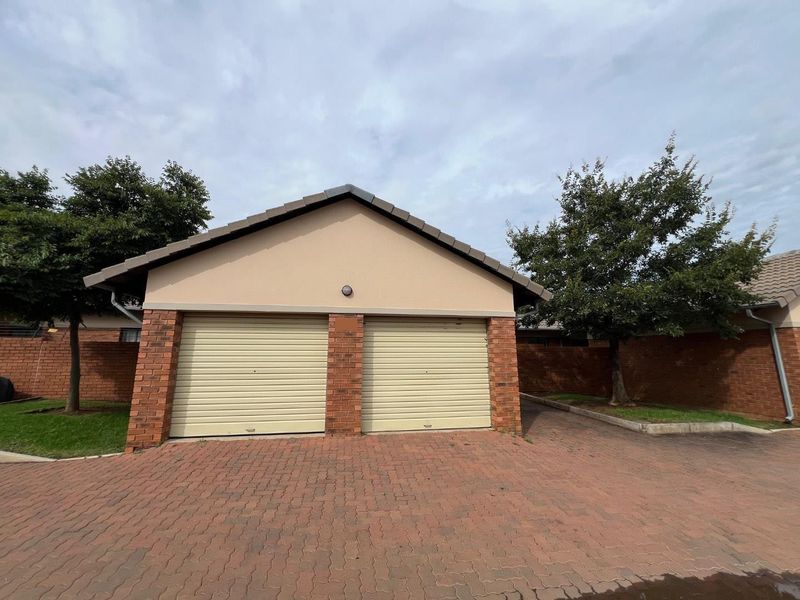 A well-maintained double garage featuring brick detailing, roller doors, and a paved driveway in a neat residential setting.