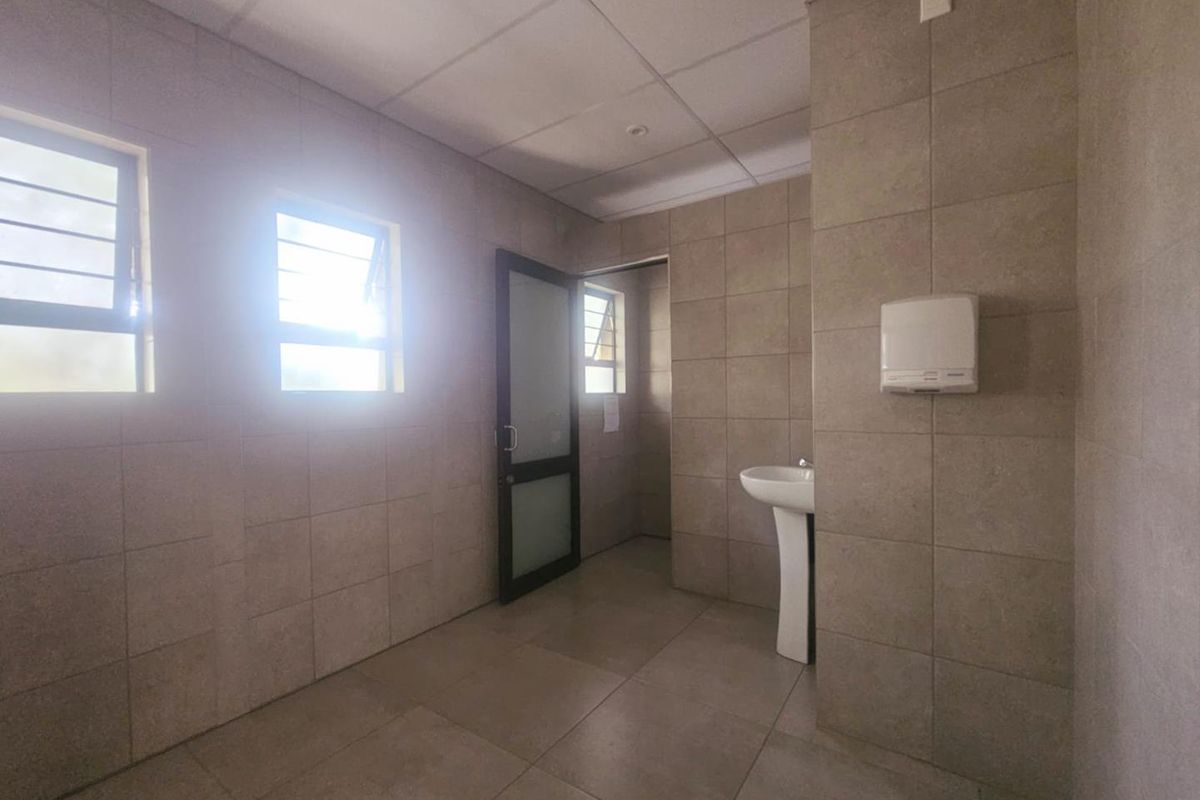A functional commercial restroom featuring tiled walls and flooring, a pedestal basin, and a paper towel dispenser.