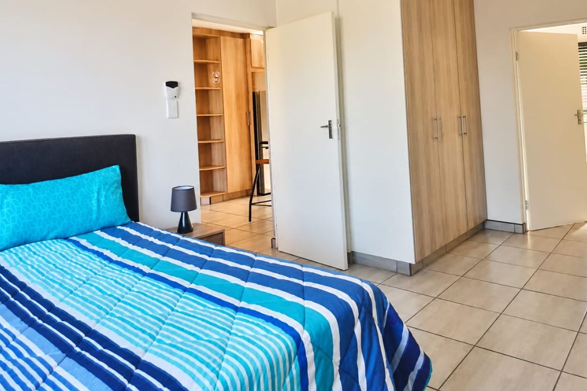 A well-maintained bedroom featuring tiled flooring, built-in cupboards, and direct access to an en-suite bathroom and adjacent storage area.