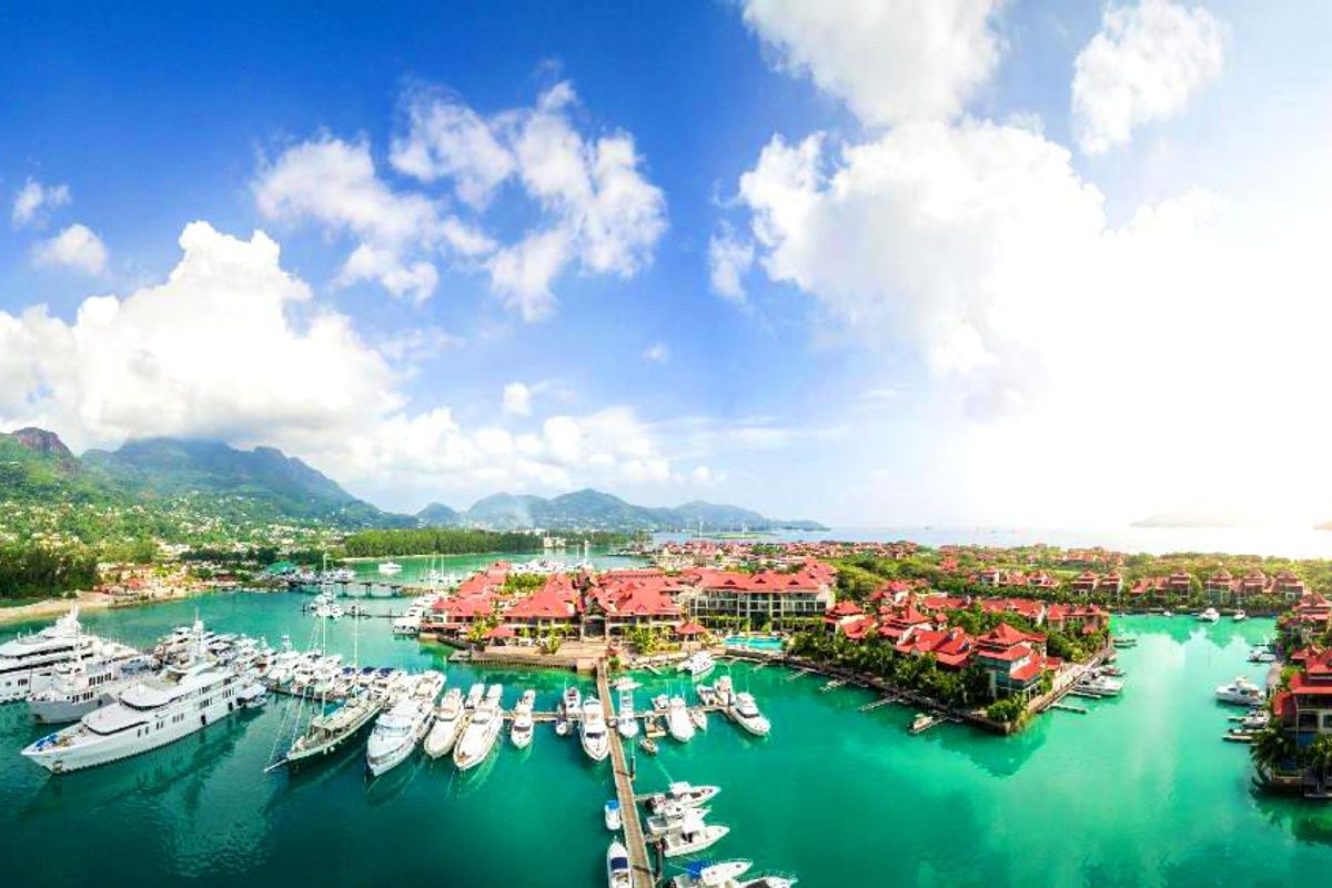 An expansive aerial view of a luxury marina and residential complex featuring turquoise waters, numerous yachts, and tropical island scenery.