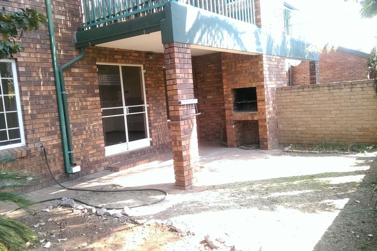 Rear exterior view featuring a brick facade, a covered patio area with a built-in braai, and access to the garden via sliding glass doors.