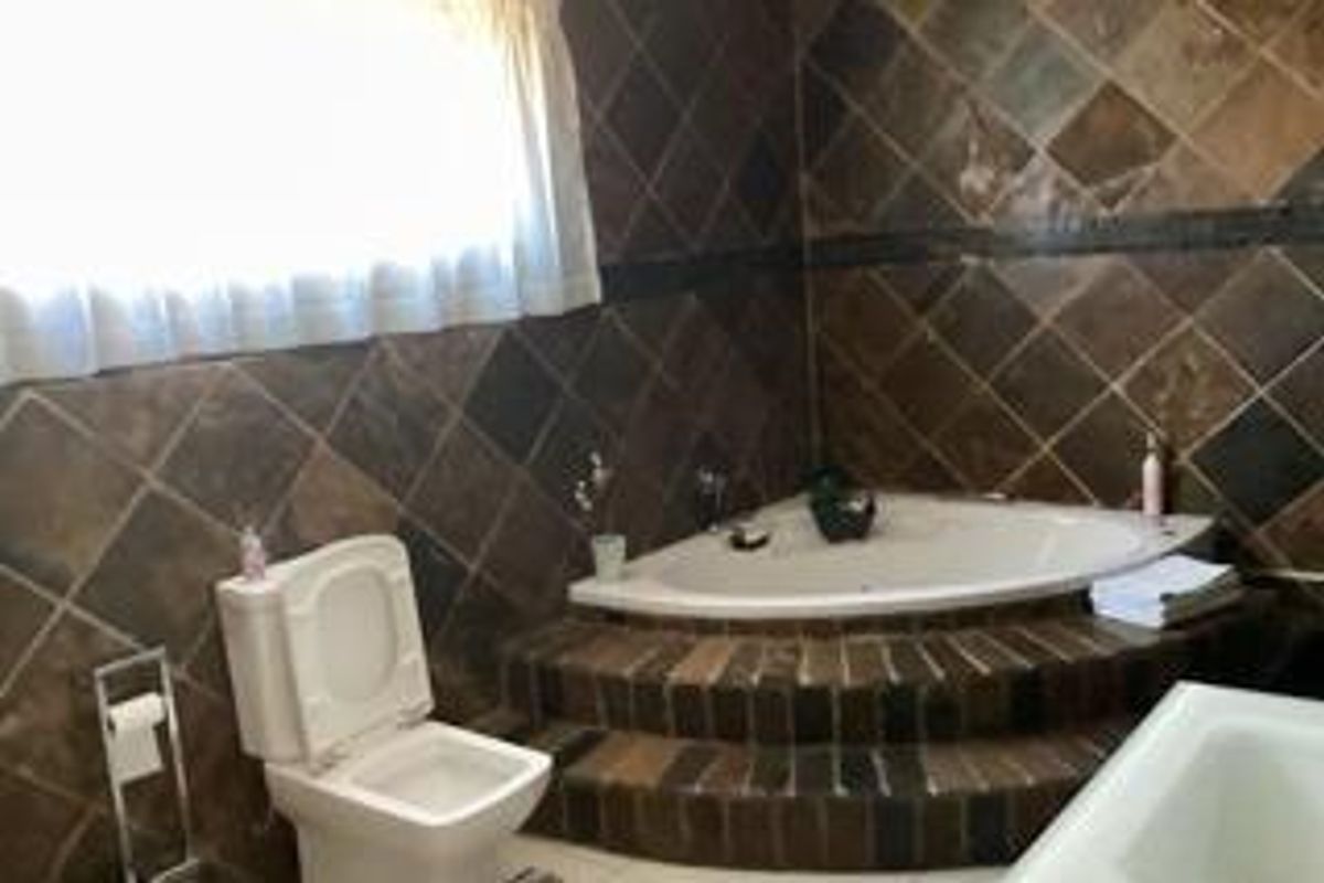 A dated bathroom featuring a corner bathtub set on a raised brick platform with dark diamond-patterned wall tiles and a standard toilet.