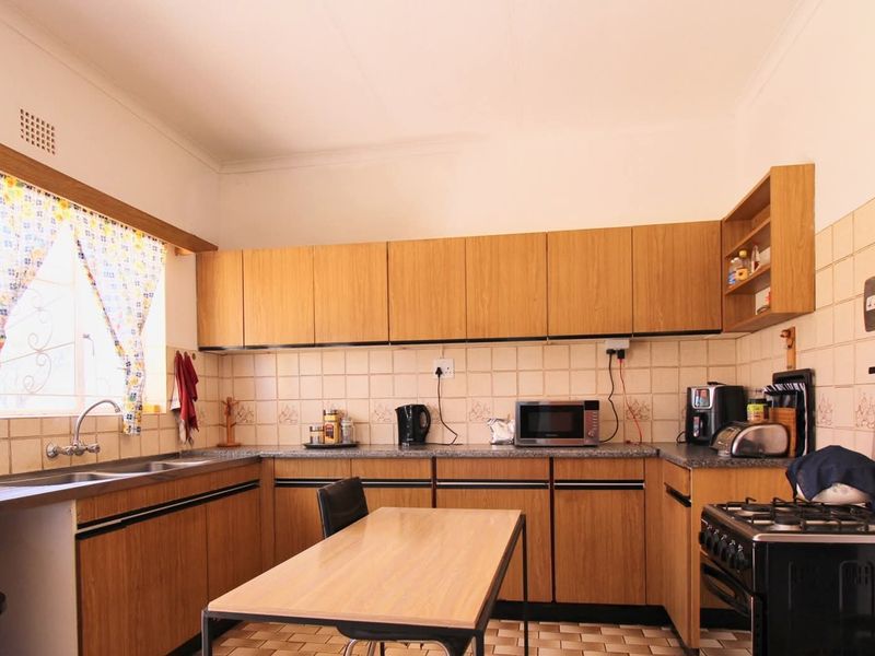 A functional kitchen featuring wood-look laminate cabinetry, tiled splashbacks, and a freestanding gas stove, offering a practical layout with ample storage space.
