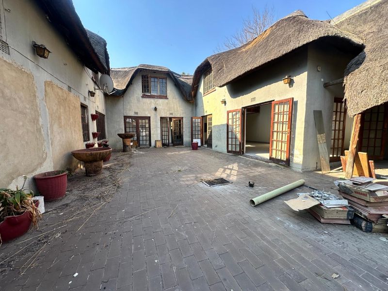 Spacious rear courtyard featuring traditional thatched roofing, brick paving, and multiple access points through timber-framed French doors, offering significant potential for outdoor renovation.