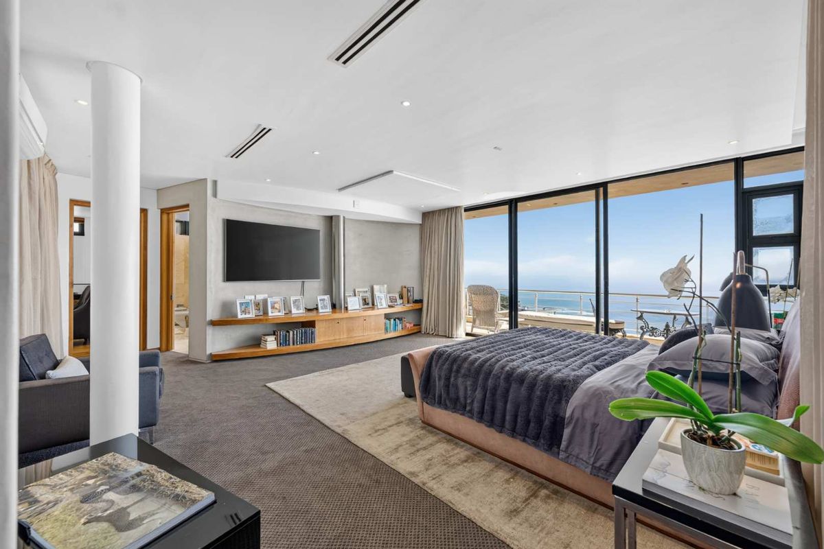 Spacious master bedroom featuring modern recessed lighting, built-in timber shelving, and expansive sliding glass doors offering panoramic ocean views.