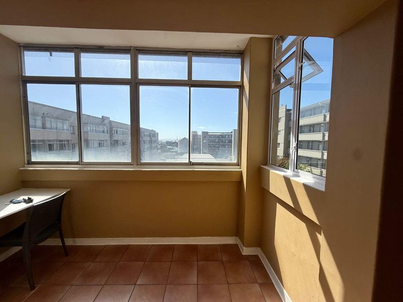 Enclosed balcony or sunroom featuring tiled flooring, aluminium window frames, and a built-in desk, offering an urban view.