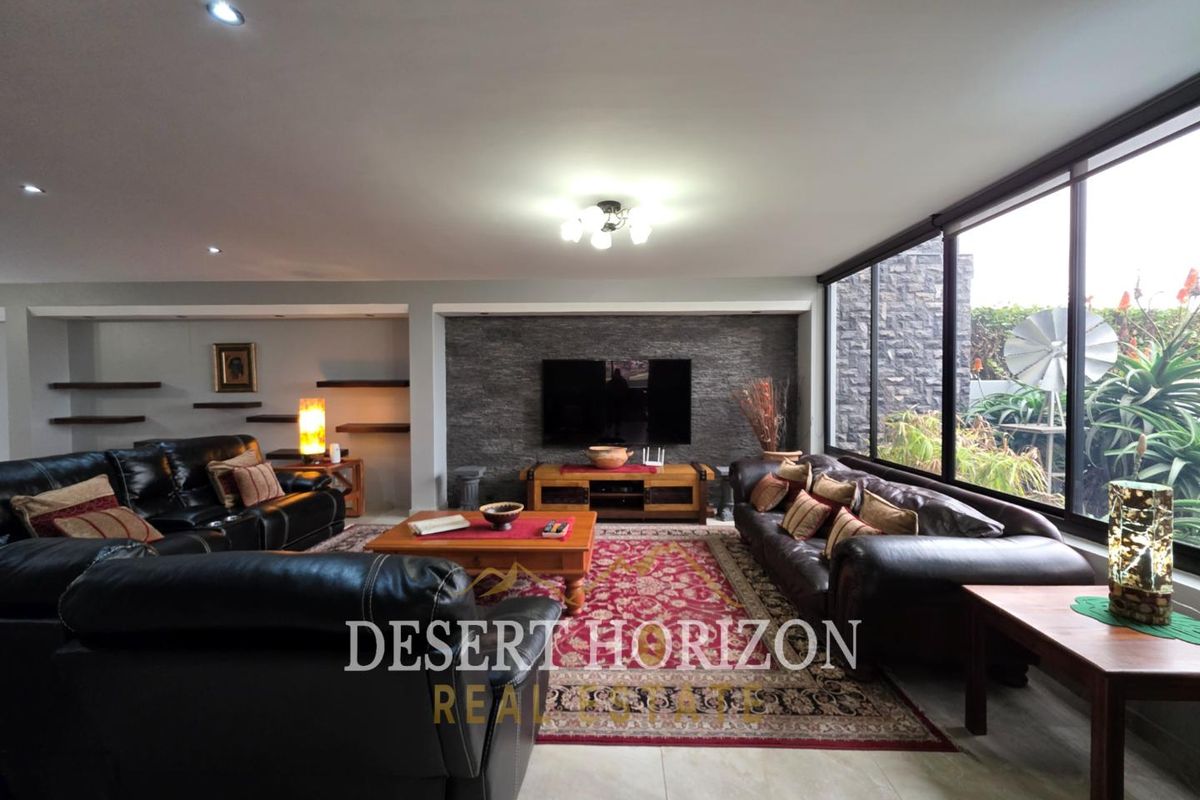 Spacious living room featuring a stone-clad feature wall, large floor-to-ceiling windows, recessed downlighting, and tiled flooring.