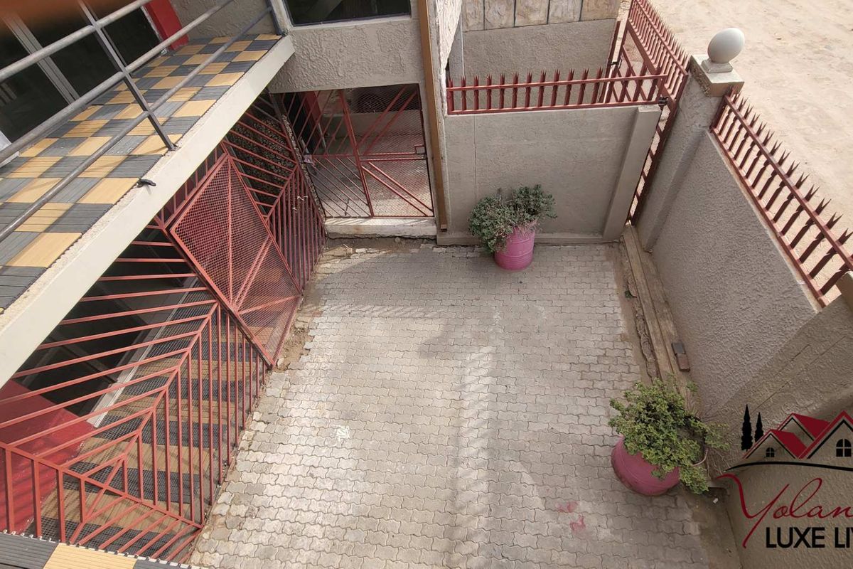 A paved rear courtyard area featuring metal security gates, perimeter walling with spikes, and an elevated tiled balcony overlooking the space.